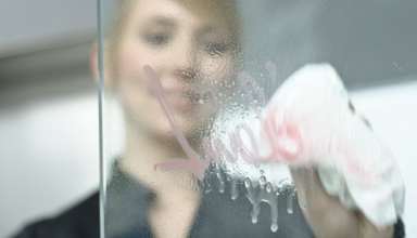 junge geschäftsfrau reinigt glasscheibe mit lappen in büro