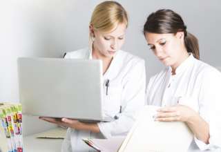 Zwei junge Ärztinennen mit Laptop und Krankenakten