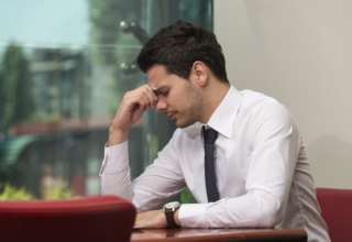 Junger Mann sitzt gestresst im Büro